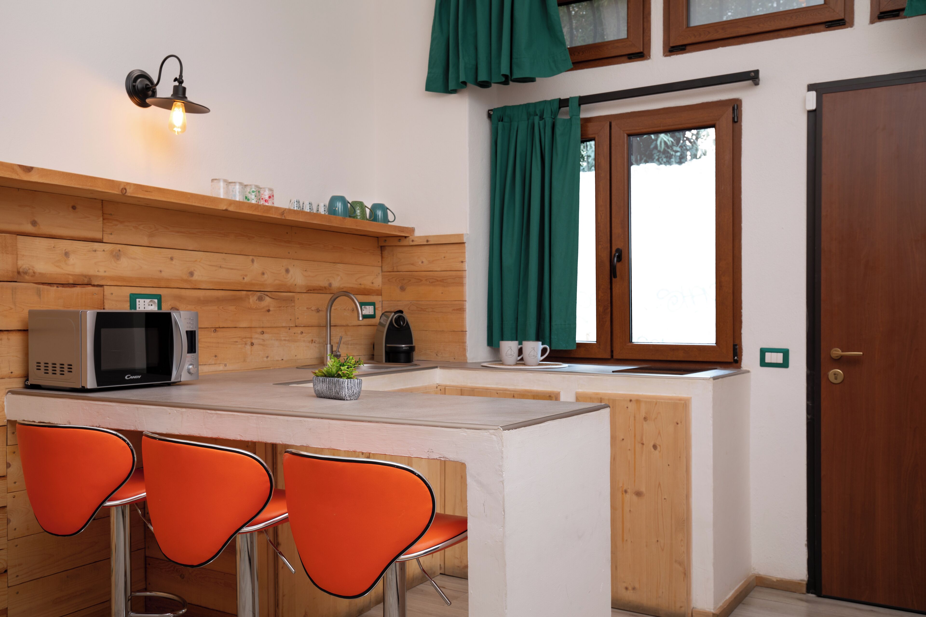 Una cocina pequeña equipada con microondas, hervidor y taburetes de bar.