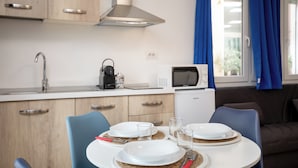 A compact kitchen with a microwave, kettle, and a sink. There is a dining table set with plates and glasses. - OlbiaLoft (Olbia)