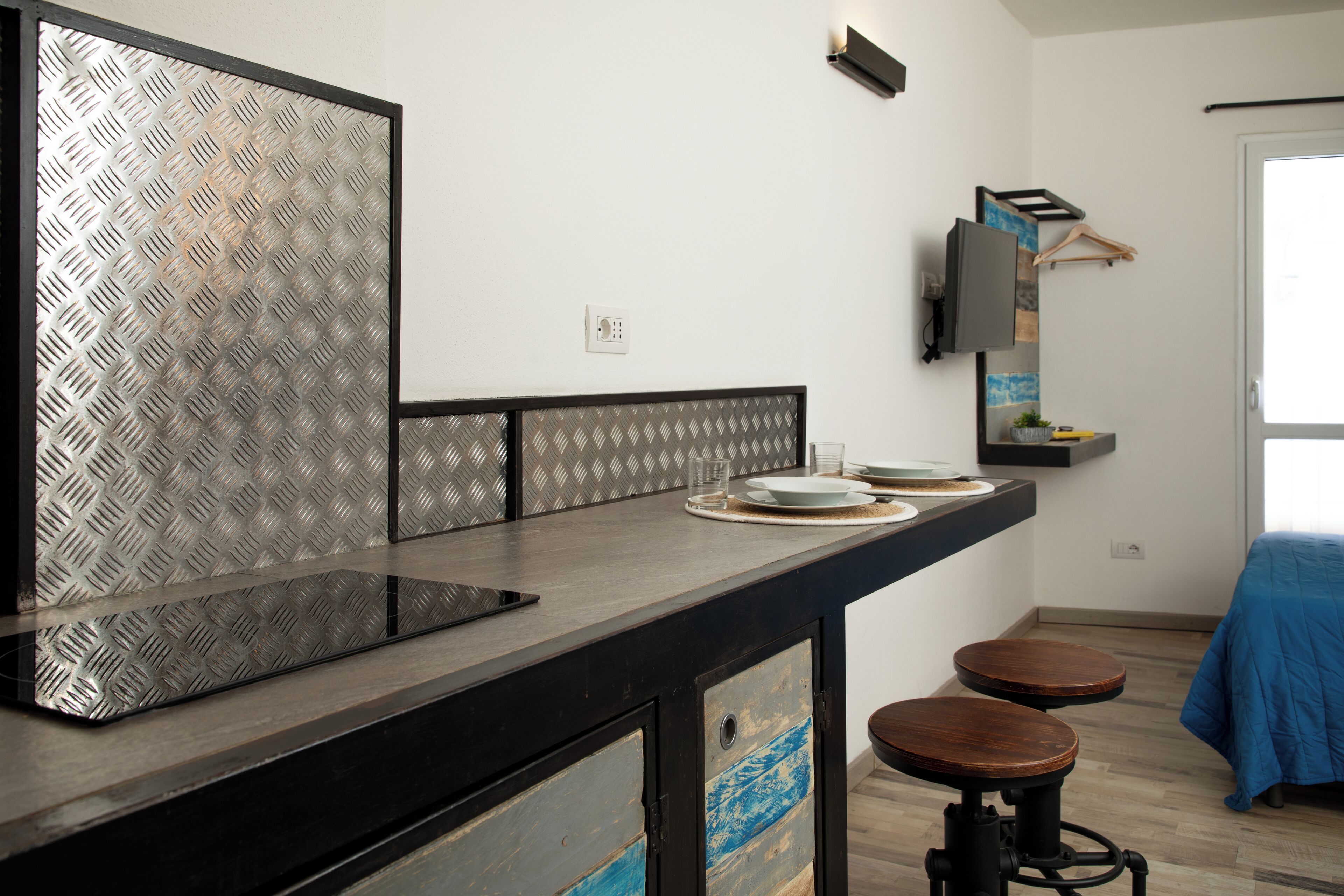 Una cocina moderna con encimera negra, lavavajillas y fregadero. Hay dos taburetes y una pequeña mesa con mantel azul.
