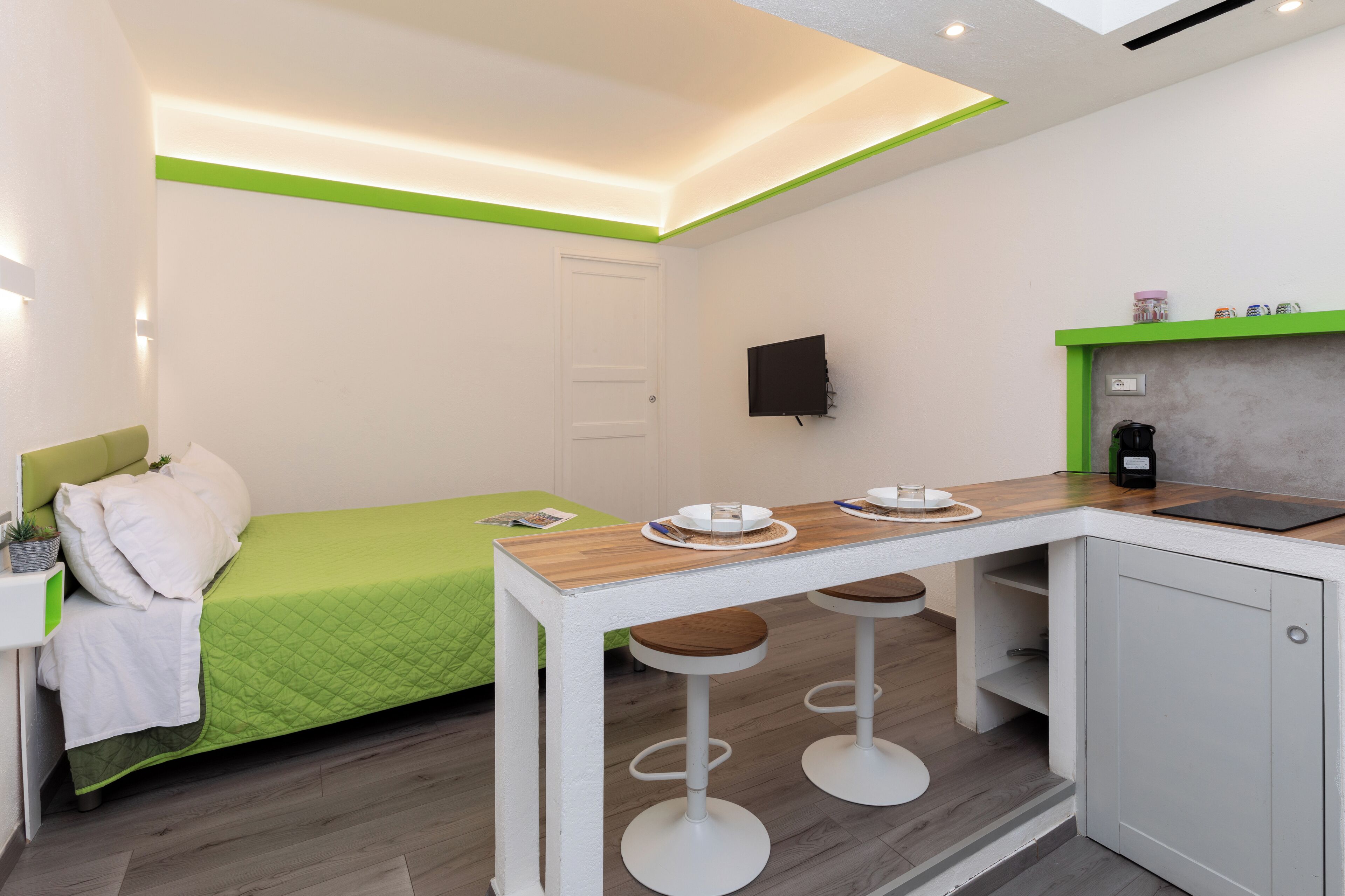 Una stanza compatta con un letto, un angolo cottura e un'area pranzo con sgabelli.