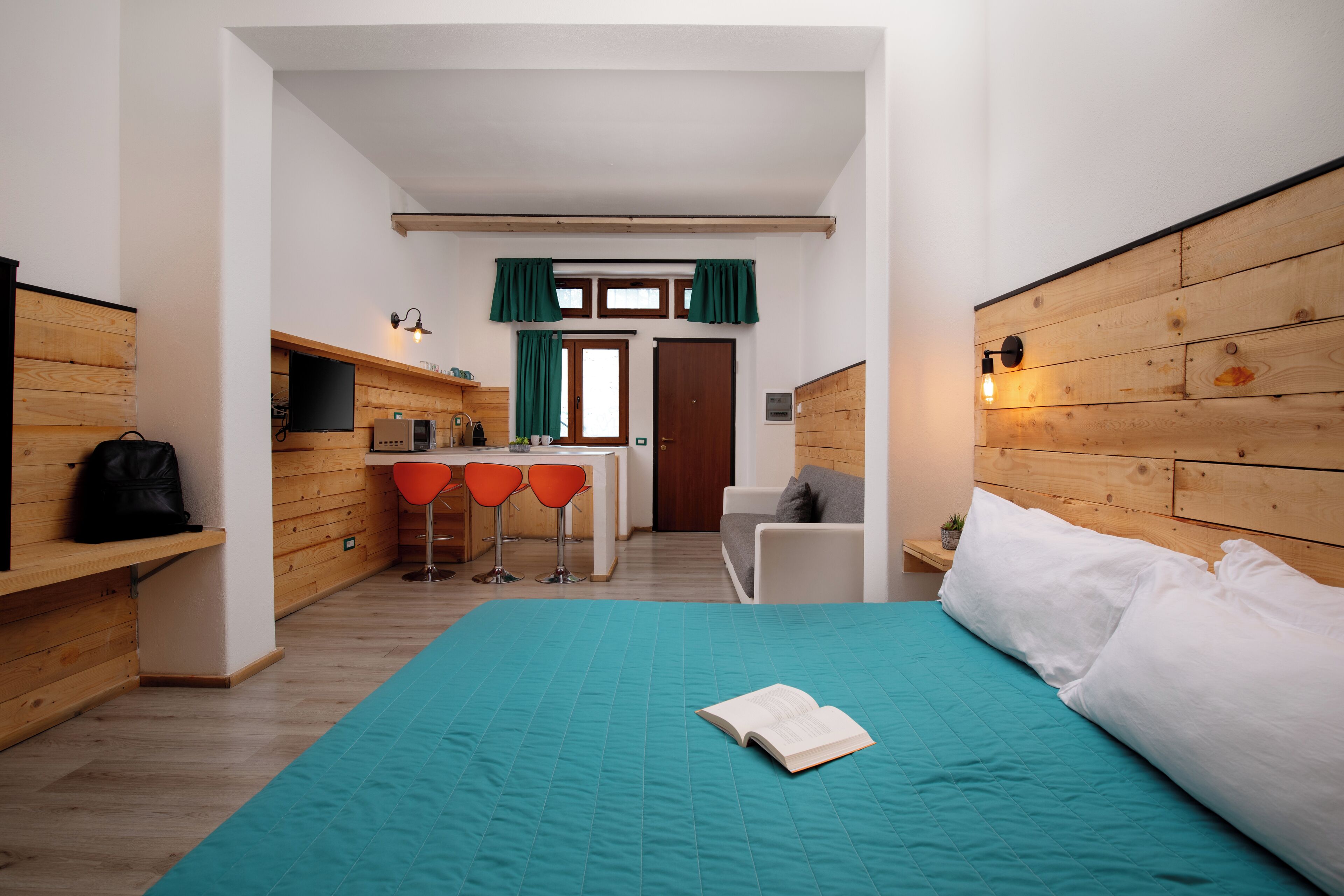 Una habitación con una cama, un escritorio con una silla, una mesita con dos sillas y una puerta.