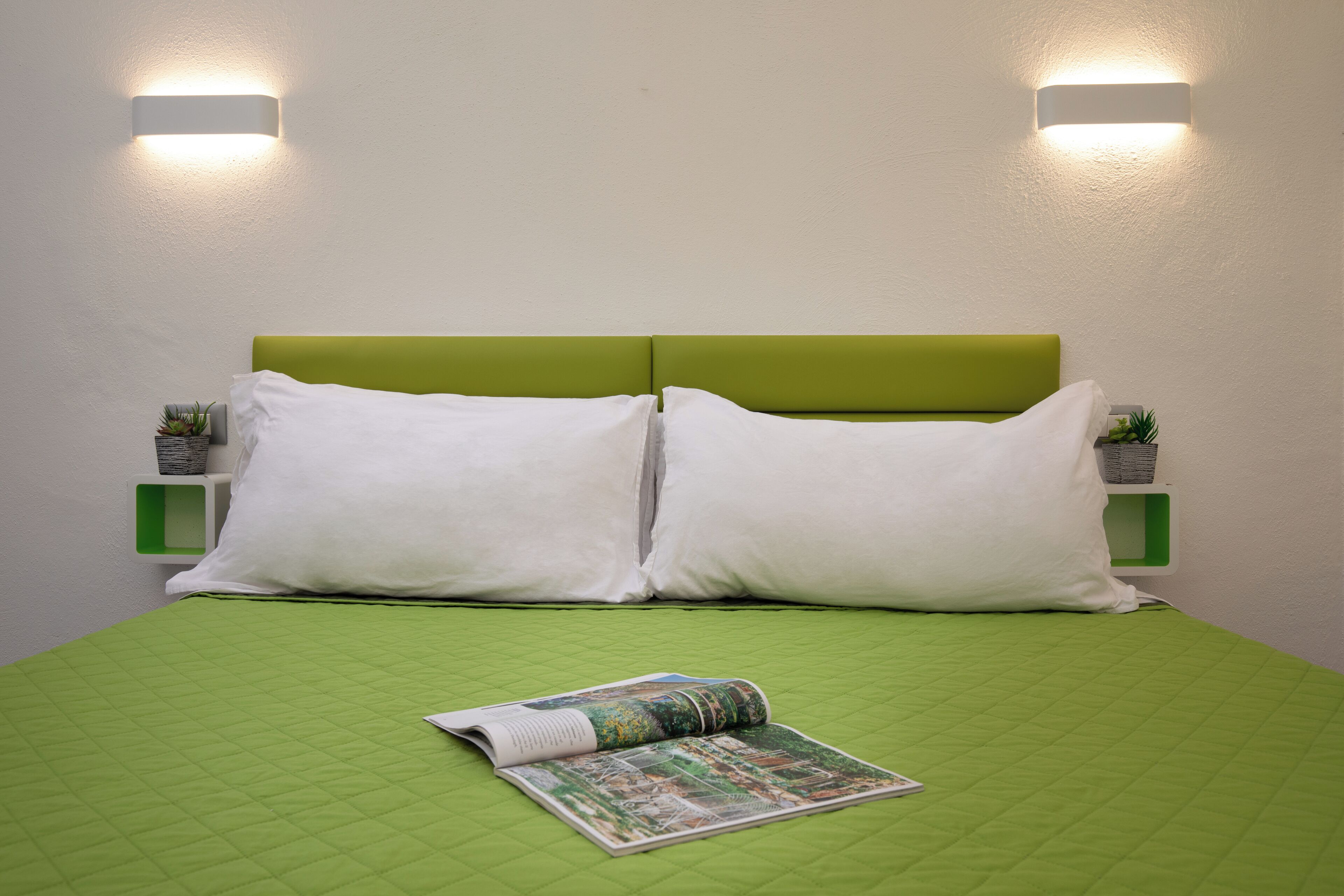 A neatly made bed with a green quilt, two white pillows, and a magazine on the bed.