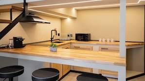 A modern kitchen with a wooden countertop, black bar stools, a microwave, and a coffee machine. - OlbiaLoft (Olbia)