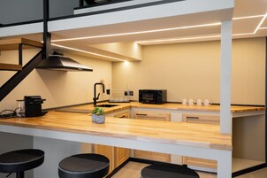 Une cuisine moderne avec un plan de travail en bois, des tabourets de bar noirs, un four à micro-ondes et une machine à café.