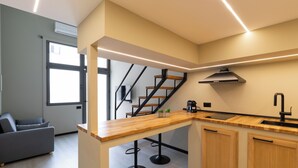 A modern kitchen with a wooden countertop, black stools, a built-in stove, and a view of a staircase leading to a balcony. - OlbiaLoft (Olbia)
