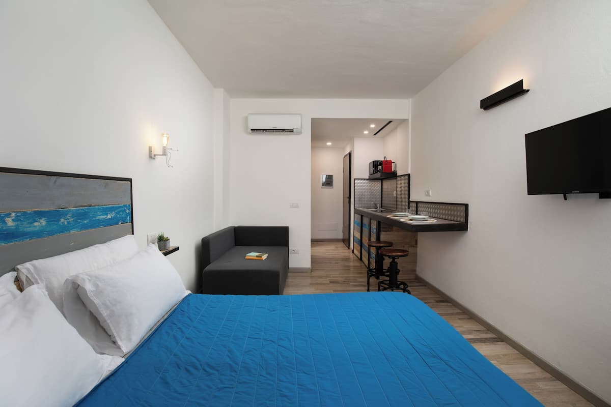 Ein modernes Hotelzimmer mit einem großen Bett, einer kleinen Sitzecke, einer Küchenzeile und einem an der Wand montierten Fernseher.