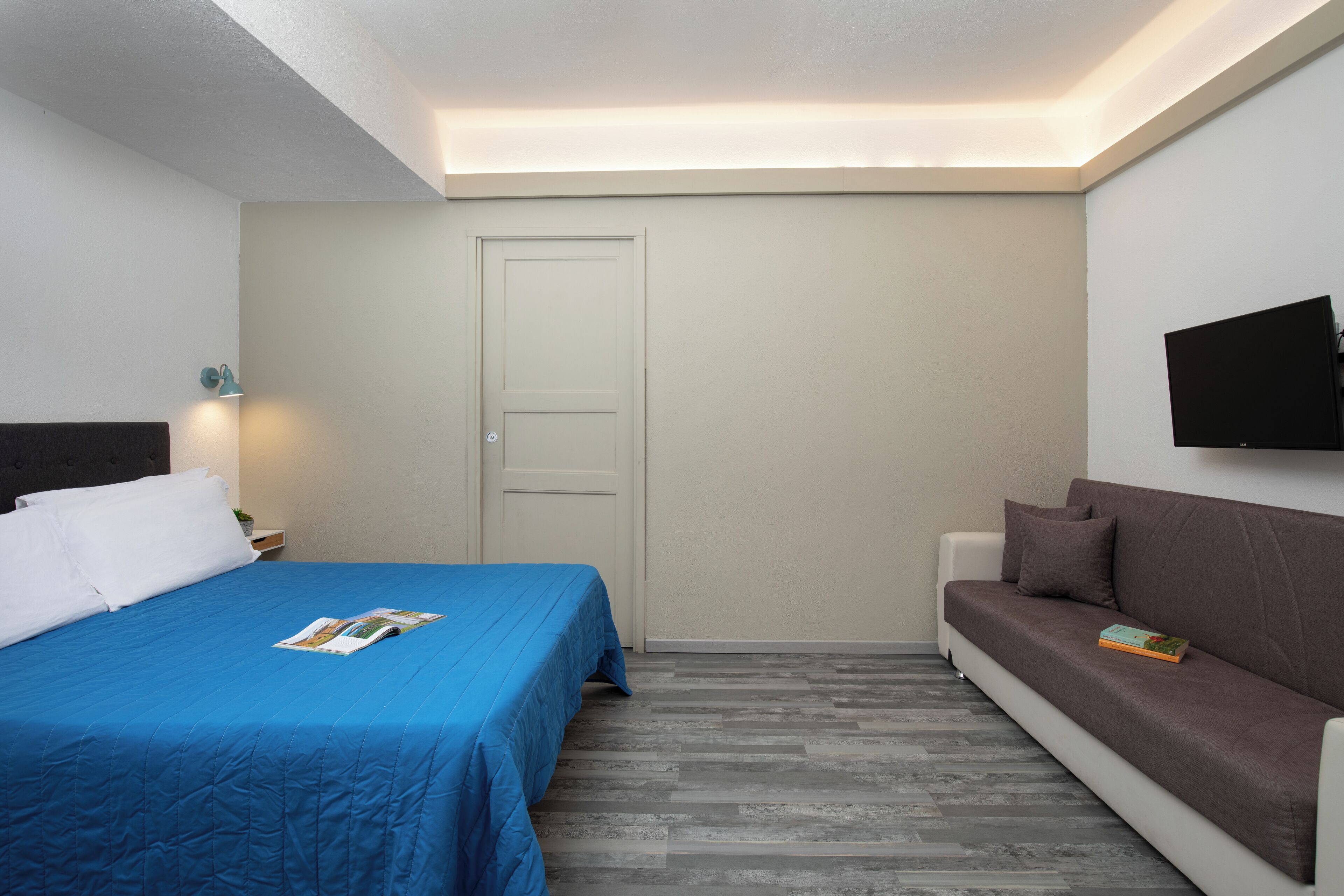 A bedroom with a bed, a sofa, a TV mounted on the wall, and a door.