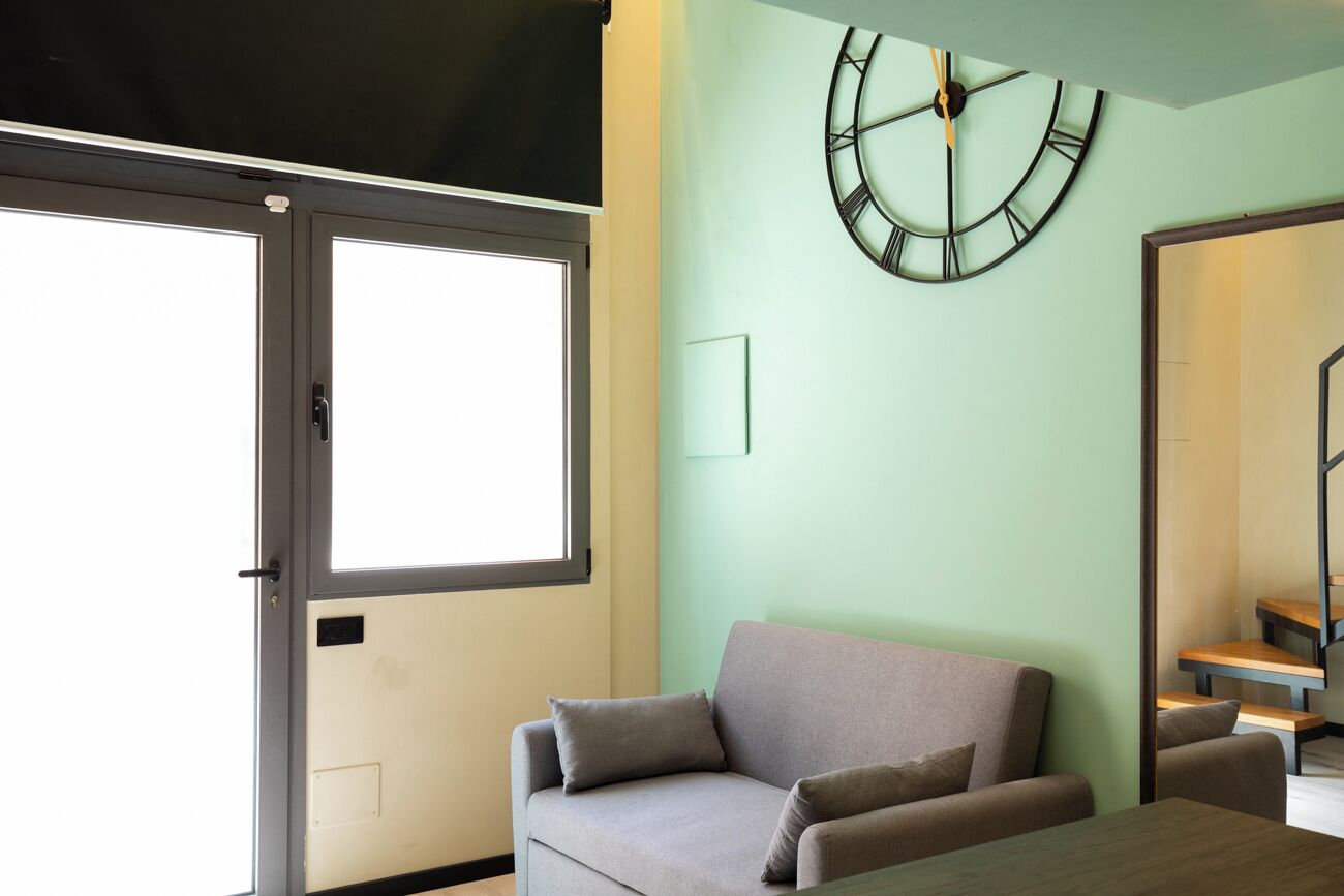 Ein Zimmer mit einer Couch, einer Wanduhr und einem Fenster.