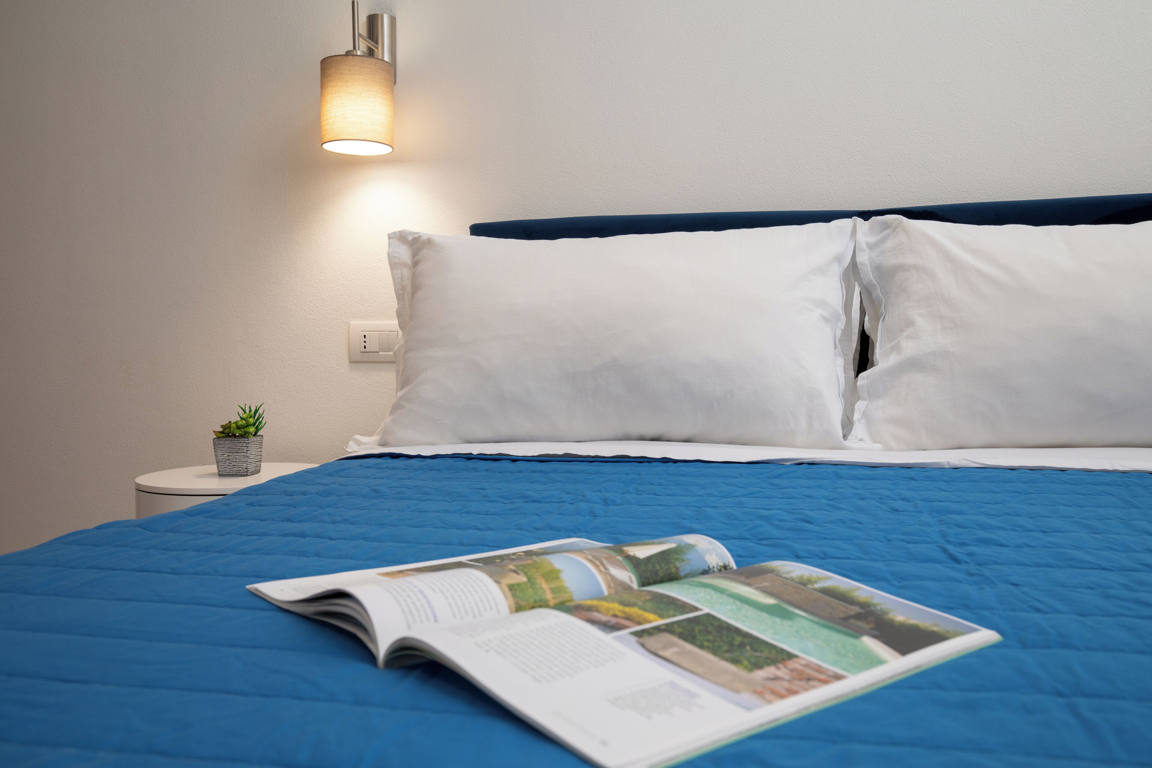 A neatly made bed with a blue bedspread, white pillows, and a magazine on the bed.