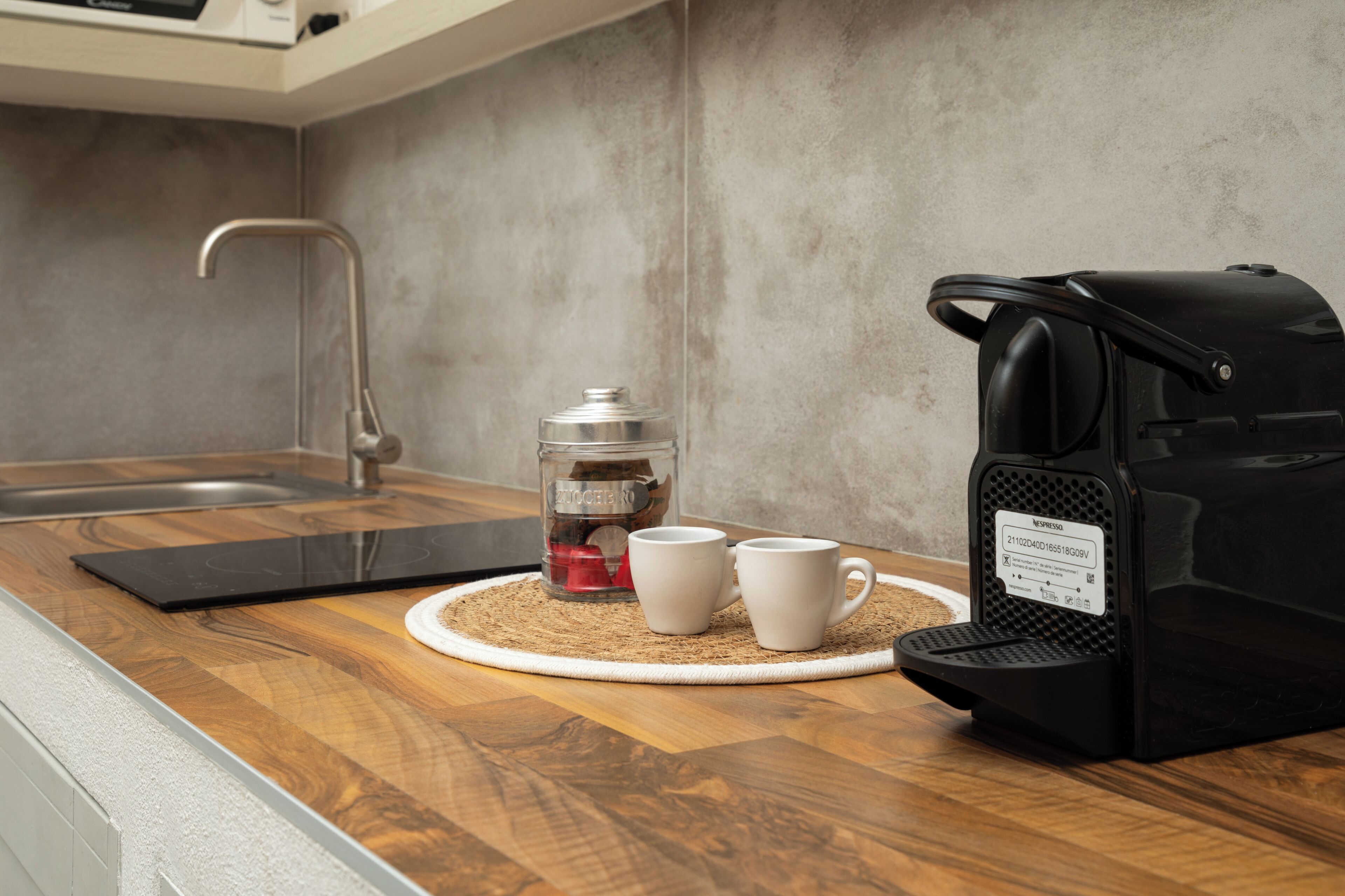 Una cocina con cafetera, dos tazas blancas y un recipiente de vidrio sobre una encimera de madera.