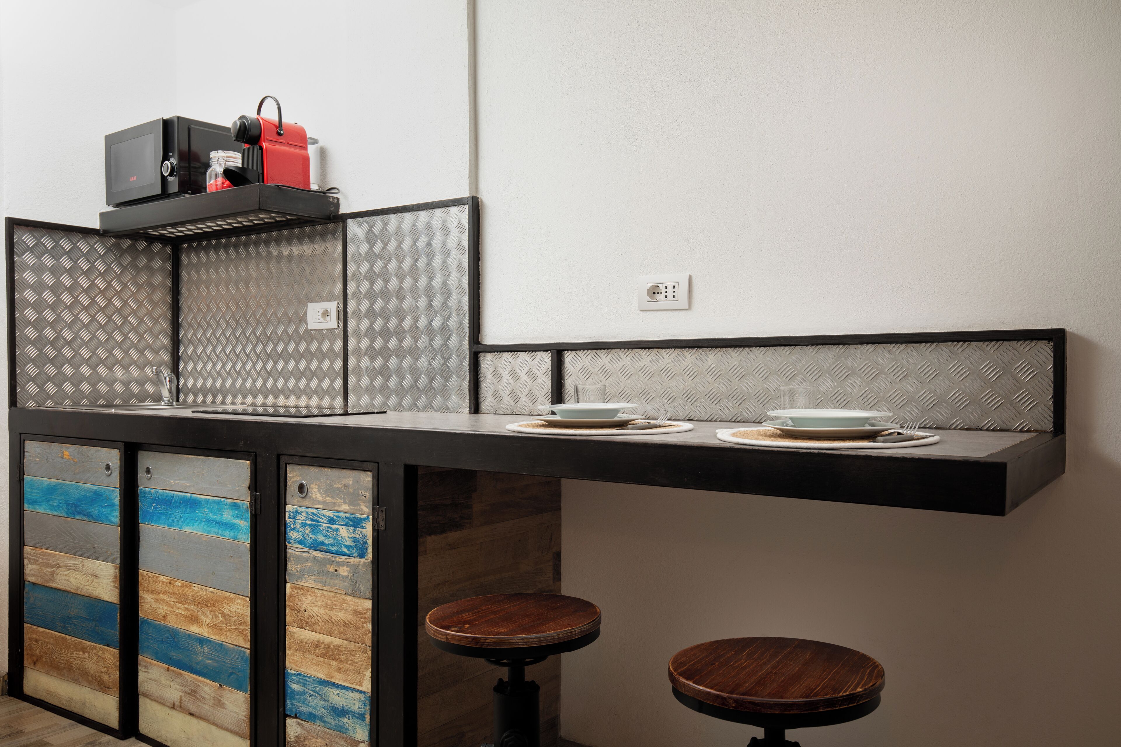 A kitchen with a black countertop, two stools, and a microwave on top.