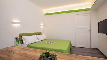 Una camera da letto moderna con una coperta verde, un comodino in legno con una pianta, una porta bianca e un televisore a schermo piatto montato a parete.