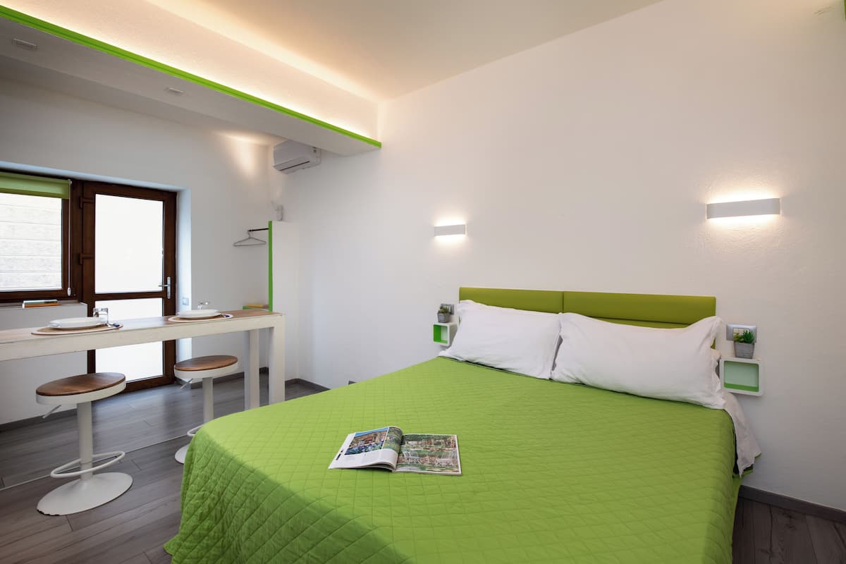 Ein modernes Hotelzimmer mit einer grünen Bettdecke, einer Zeitschrift auf dem Bett, einem Schreibtisch mit Hocker und einem Fenster mit Blick.