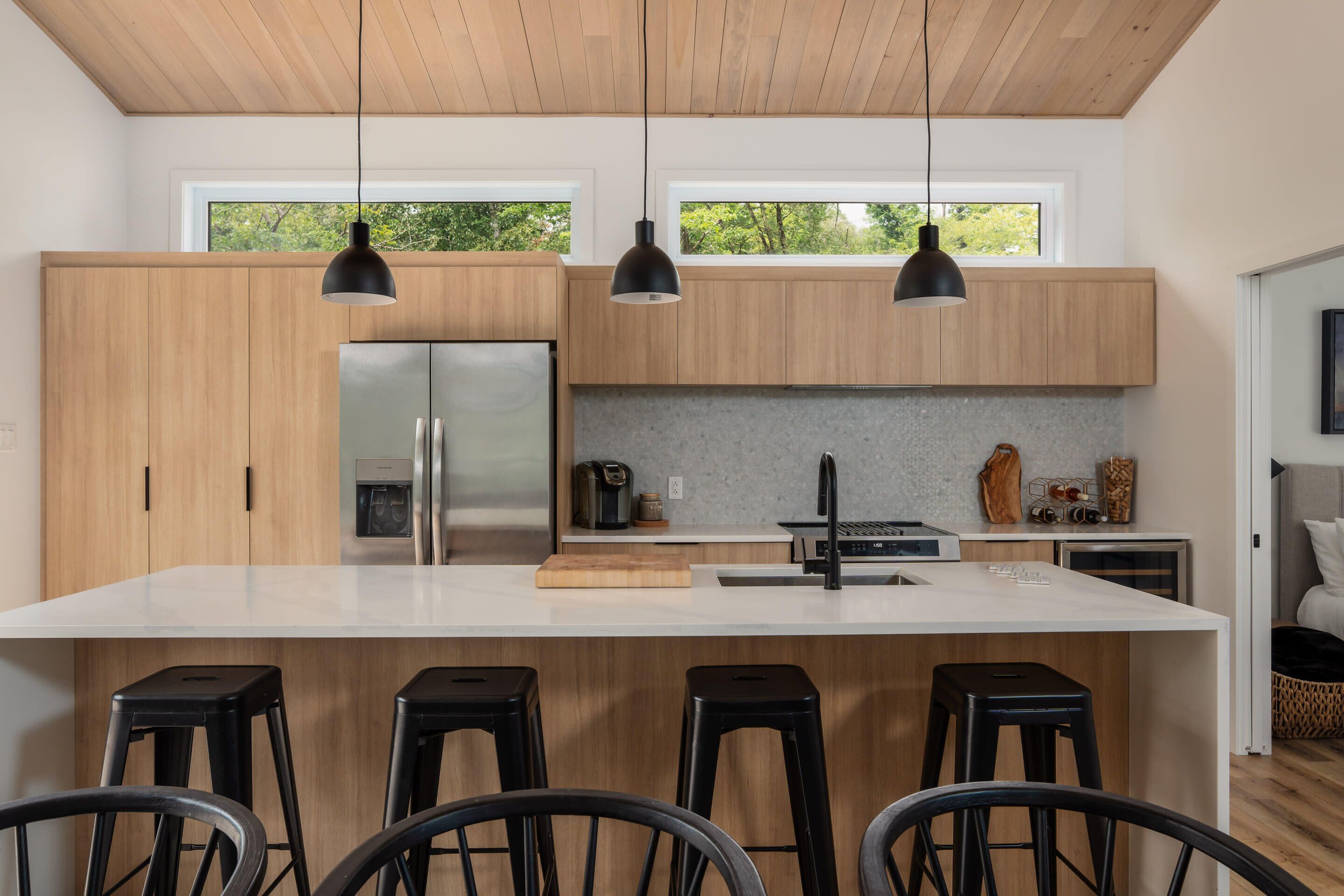 A modern kitchen with wooden cabinets, a large island with stools, and pendant lighting.