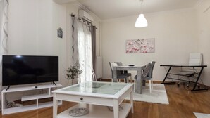 Un salon moderne doté d’un téléviseur à écran plat, d’une table basse avec un plateau en verre, d’un coin repas avec une table et des chaises, et d’un bureau debout avec un siège.