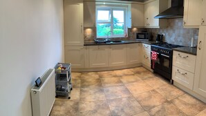 A kitchen with white cabinets, a stove, a microwave, and a window with a view of greenery. - Coventry Charm - Spacious 3 Bedroom House (Coventry)