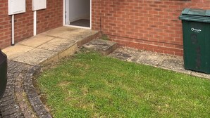A brick building with a door, windows, and a green recycling bin. - Coventry Charm - Spacious 3 Bedroom House (Coventry)