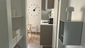 A hallway leading to a kitchen with a clock on the wall, a chair, and a small table. - Charmantes Design-appartement für 2 Personen in Utting am Ammersee (Utting am Ammersee)