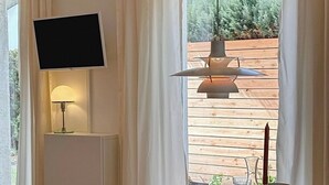 A dining area with a round table, two chairs, a TV mounted on the wall, and a window with curtains. - Charmantes Design-appartement für 2 Personen in Utting am Ammersee (Utting am Ammersee)