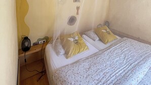 A room with a bed, a mosquito net, a shelf with a lamp, and a wall with a decorative design. - Destination for Couple, Surfers, Hikers, and Nature Lovers! (Carrapateira)