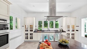 A modern kitchen with white cabinetry, a central island, and a view of greenery outside.