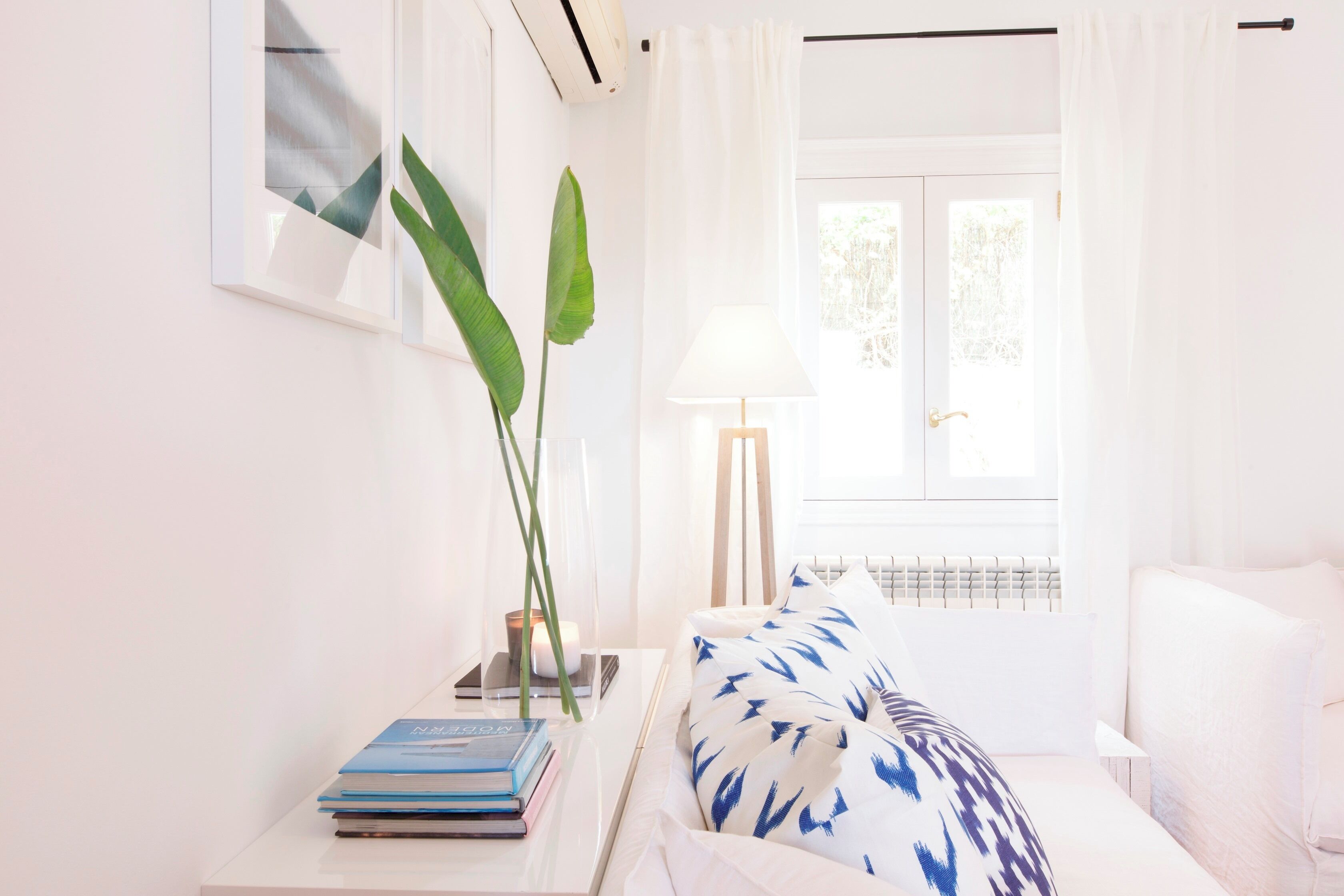 Een keurig opgemaakt slaapkamer met een bed, nachtkastje met boeken, een lamp en een raam met gordijnen.
