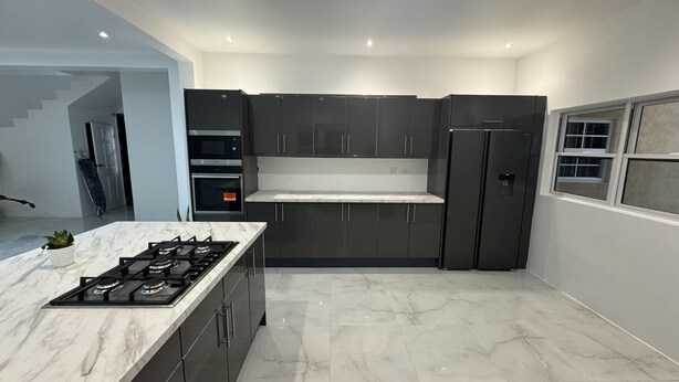 A modern kitchen with dark cabinets, a marble countertop, and built-in appliances including a stove, oven, and microwave.