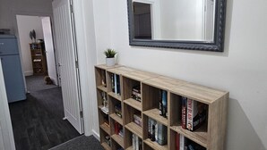 A hallway with a wooden bookshelf, a mirror, and a door leading to another room.