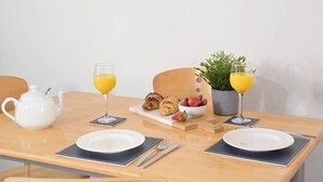 A dining table with a white teapot, two glasses of orange juice, a plate with croissants and strawberries, and a potted plant.