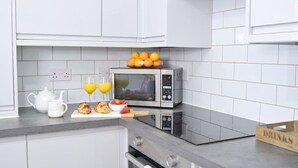 A kitchen with white cabinets, a microwave, a teapot, two glasses of orange juice, croissants, strawberries, and a box labeled "Drinks".