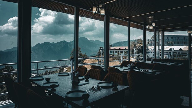 Un restaurante con grandes ventanales que ofrece vistas a montañas y un edificio distante.