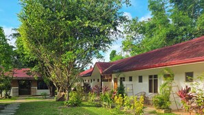 A row of white buildings with red roofs, surrounded by lush greenery and a well-maintained lawn. - Masayana Hotel (El Nido)