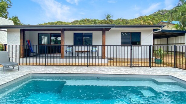 A swimming pool with a fenced deck area, a covered seating area, and a view of a hillside. - Nerita Nook (Nelly Bay)