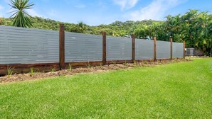 A fenced area with a grassy foreground and a backdrop of trees and hills. - Nerita Nook (Nelly Bay)