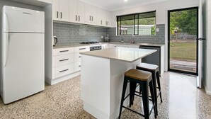 A modern kitchen with white cabinetry, a central island, and a large window. - Nerita Nook (Nelly Bay)