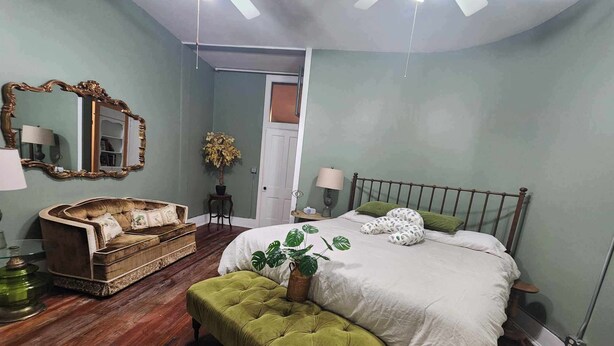Un dormitorio con una cama, un banco tapizado de color verde, un banco de madera, un espejo y una planta en maceta.