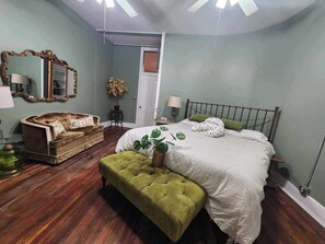 Een slaapkamer met een bed, een groene bekleden bank, een houten bankje, een spiegel en een potplant.
