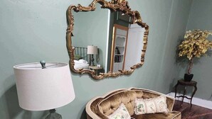 Una habitación con un sofá de estilo vintage, un espejo grande y ornamentado, una lámpara y una planta en maceta.