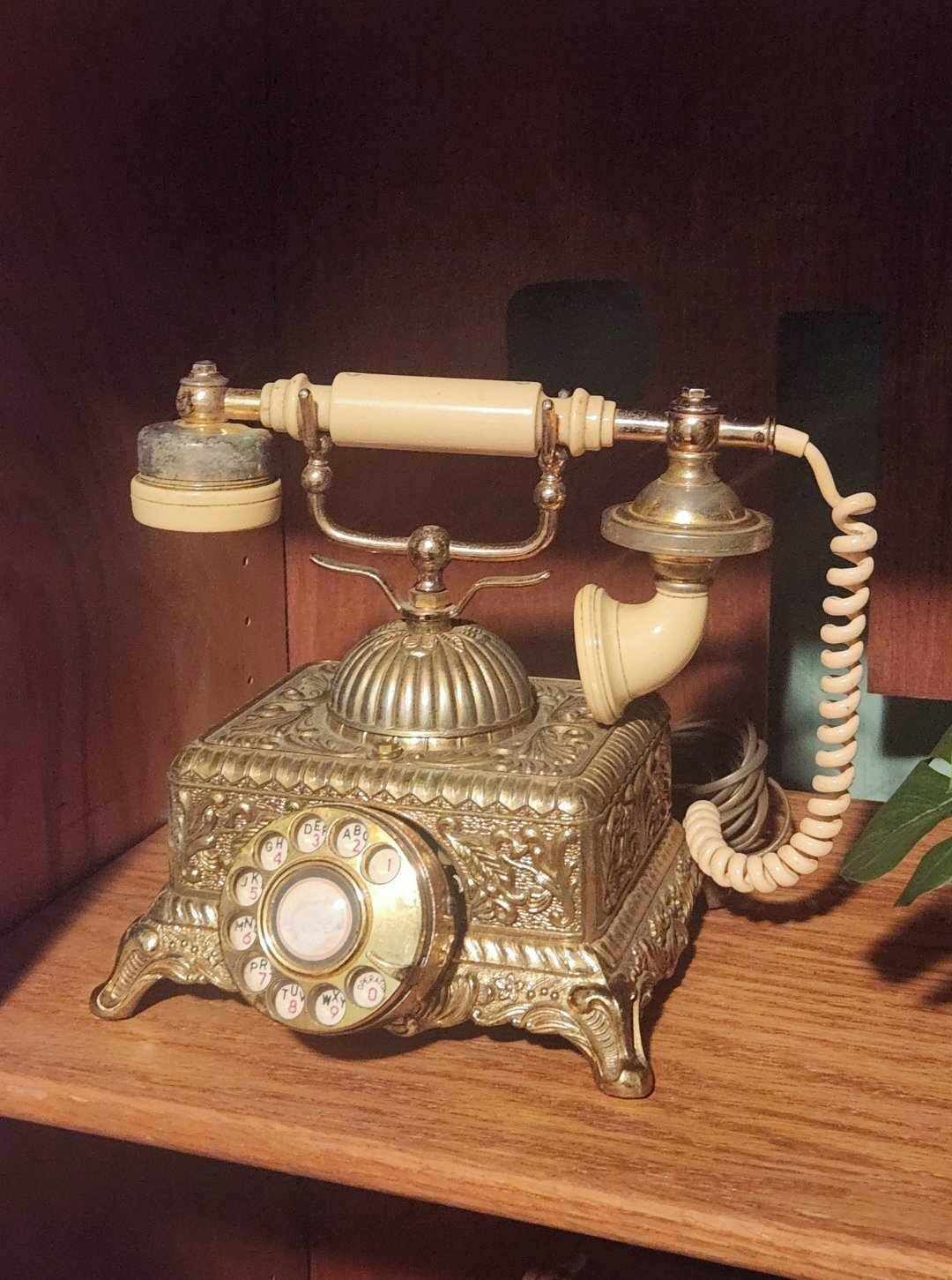 An ornate antique telephone with a rotary dial and a coiled cord, placed on a wooden surface.
