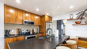 Une cuisine moderne avec des meubles en bois, des appareils en acier inoxydable, un îlot central doté de chaises et des étagères intégrées.
