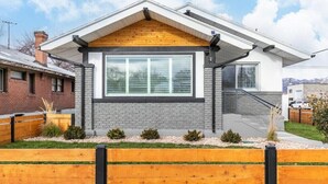 Une maison moderne à deux étages, dotée d’une grande fenêtre, d’un porche en bois et d’une façade en briques.
