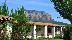 Un edificio tradicional blanco con techo de tejas, rodeado de vegetación y una montaña al fondo.