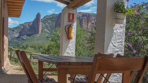 Una mesa y sillas de madera bajo un techo de madera, con vistas a montañas y un extintor en la pared.
