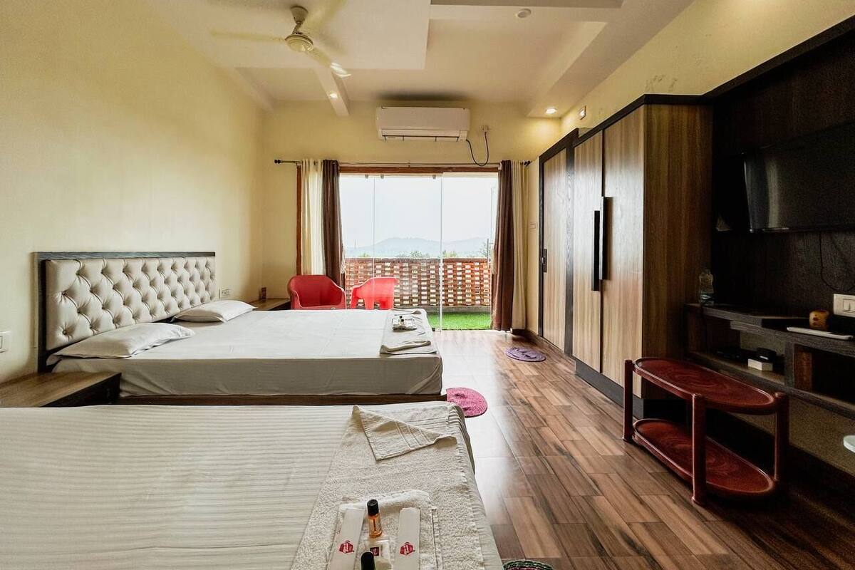 Quarto de hotel com duas camas, televisão e varanda com vista.