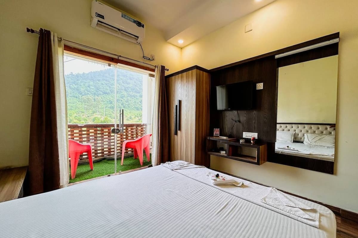 Quarto de hotel com cama, televisão, guarda-roupa e varanda com cadeiras.