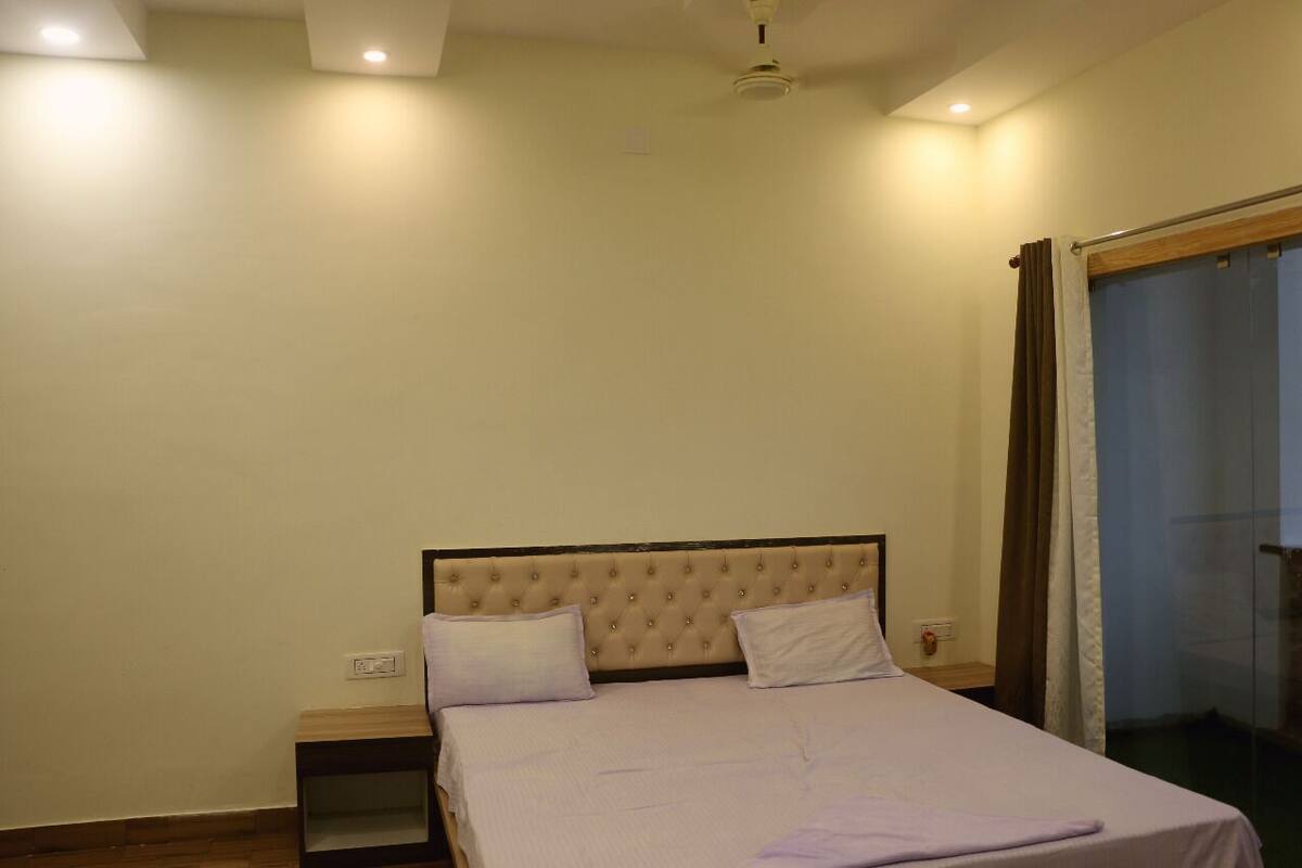 Quarto com cama, mesa de cabeceira e janela com cortinas.