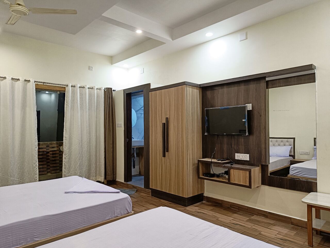 A hotel room with two beds, a wardrobe, a TV, and a mirror.