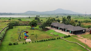 A rural landscape with a playground, a small pavilion, and a row of solar-powered buildings. - Allure De Baranti (Raghunathpur)