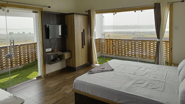 A bedroom with a large bed, a TV, and a balcony with a view of the countryside. - Allure De Baranti (Raghunathpur)