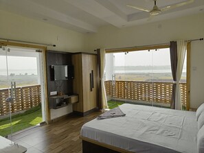 A bedroom with a large bed, a TV, and a balcony with a view of the countryside. - Allure De Baranti (Raghunathpur)